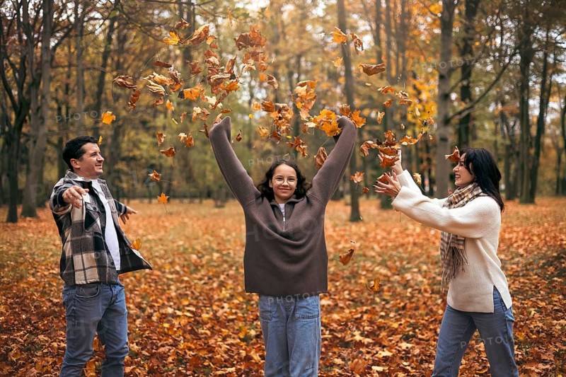 A joyful family playing in a park, tossing vibrant autumn leaves. The scene captures the spirit of togetherness and fun on a crisp fall day surrounded by colorful foliage