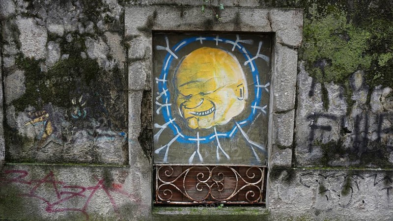 Graffiti of a yellow face on an old, painted wall in an urban environment, hiking on the Caminho Portugues da Costa, Portugal