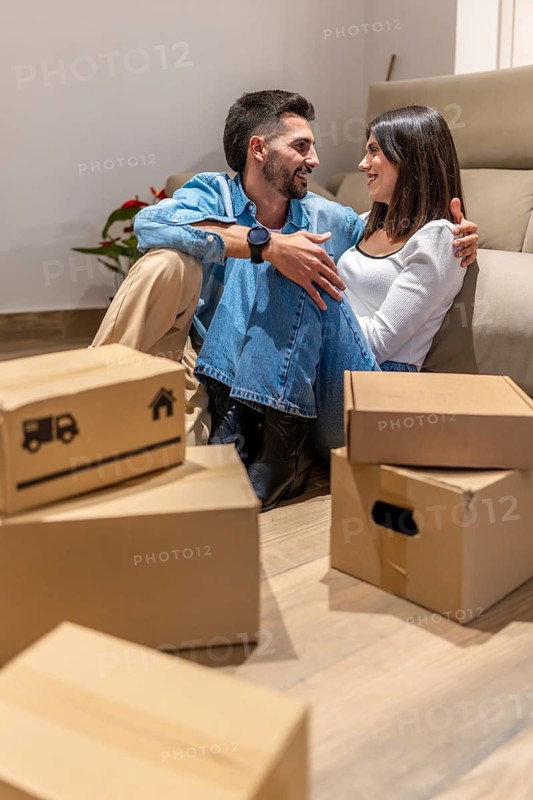 Young couple smiling and enjoying a moment of relaxation while taking a break from unpacking cardboard boxes in their new home