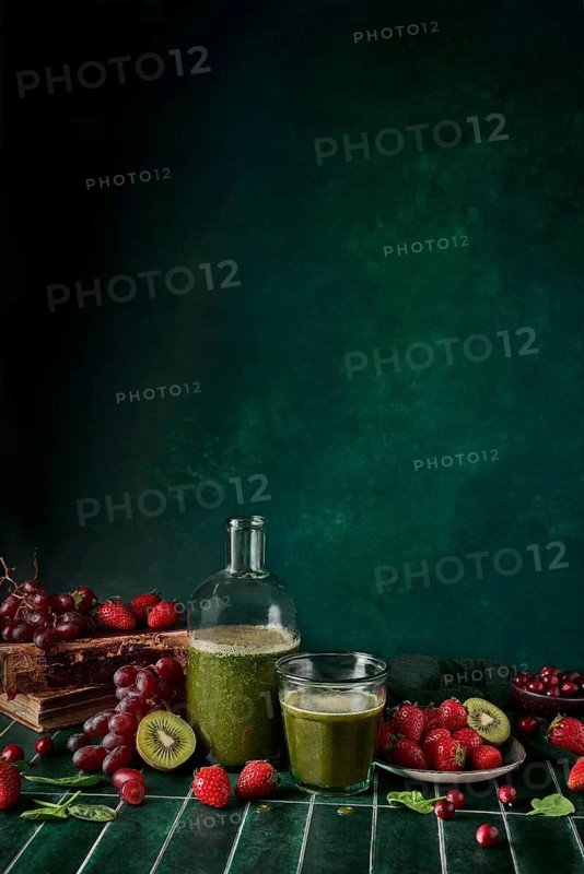 A refreshing green spinach juice in a glass bottle with a cup, surrounded by fresh strawberries, cherries, and grapes. Perfect for a health-conscious lifestyle and vibrant energy