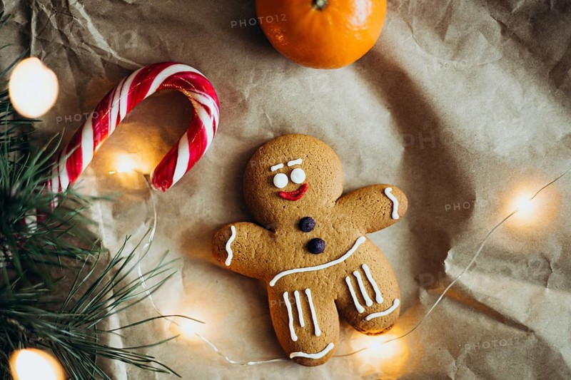 A cheerful gingerbread man cookie is surrounded by a candy cane, orange, and warm glowing lights Perfect for celebrating the festive holiday season with sweetness and style
