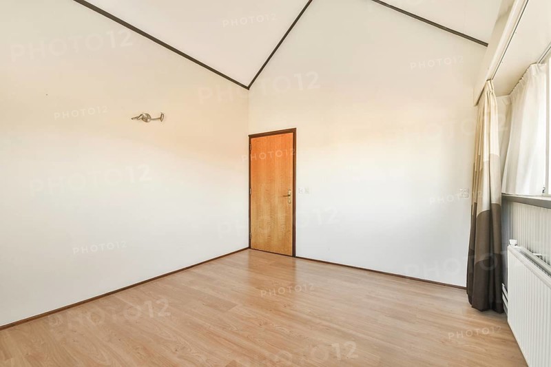 A clean and simple interior featuring wooden flooring, a door, and large windows allowing natural light to flood the room, creating a serene atmosphere