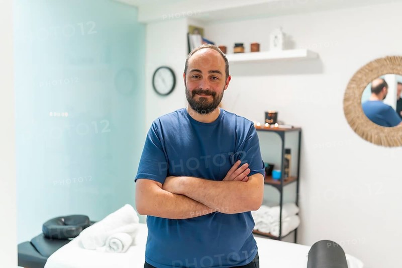 Male professional masseur standing with crossed arms in a bright wellness spa clinic, providing relaxing and therapeutic services for health and well being