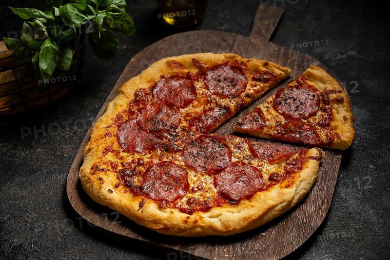 A mouth watering homemade pepperoni pizza sits on a rustic wooden board, surrounded by fresh basil leaves. Perfectly baked, it exudes an inviting aroma, promising a savory delight