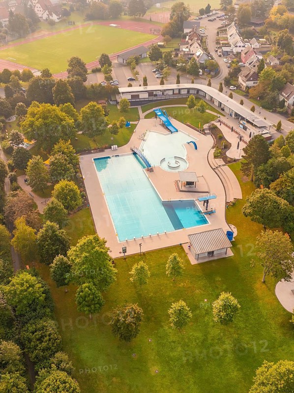 A swimming pool with outdoor area, surrounded by green spaces and trees, in an urban environment photographed from the air, Calw, Black Forest, Germany