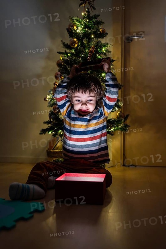 A young boy is sitting in front of a Christmas tree with a red box in front of him