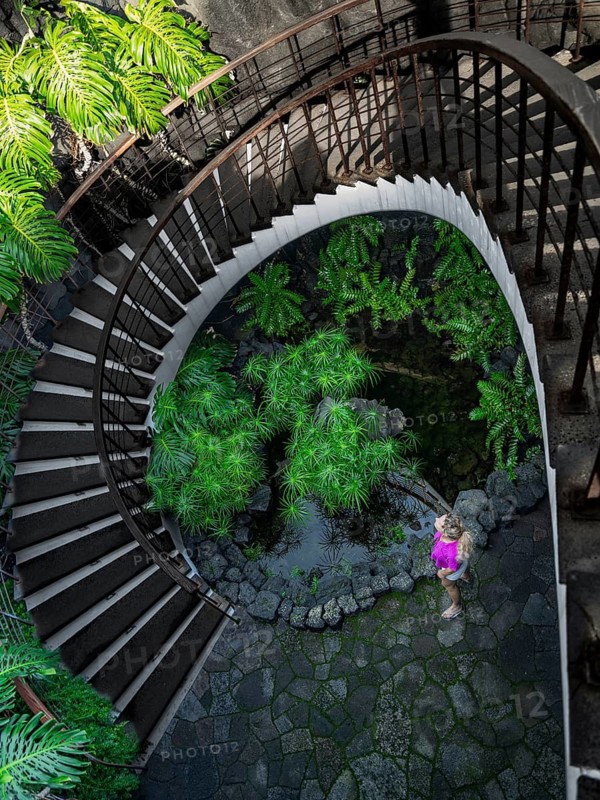 A woman tours an enchanting garden oasis beneath a spiral staircase while on holiday in Lanzarote, Canary Islands, Spain
