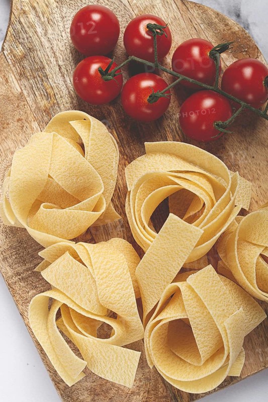 Raw pappardelle pasta, on a wooden chopping board, with cherry tomatoes, top view, no people
