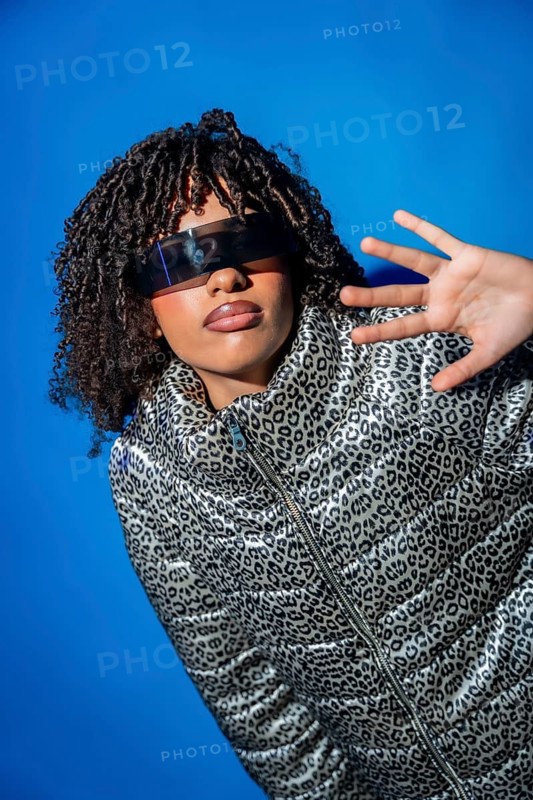 Stylish model showcasing futuristic eyewear and a trendy animal print jacket against a vibrant blue backdrop