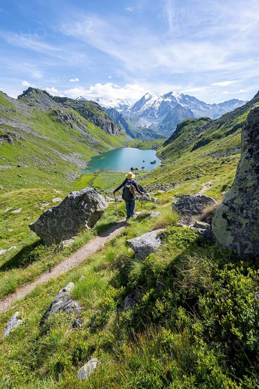 Mountaineer on hiking trail in picturesque mountain landscape, view of mountain lake Lac du Louvie and glaciated mountain peaks of the Grand Combine, Valais Alps, Val de Bagnes, Valais, Switzerland