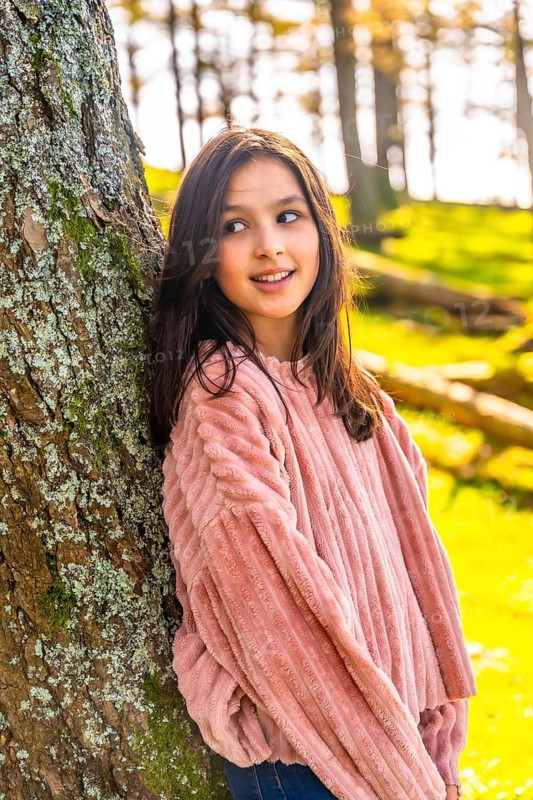 Vertical side view portrait of a caucasian cute girl leaning in a tree trunk in the forest