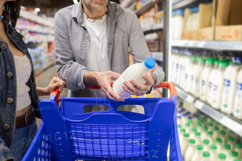 A couple carefully selects a bottle of milk while shopping together in a supermarket. They examine the product before adding it to their cart, surrounded by various dairy items