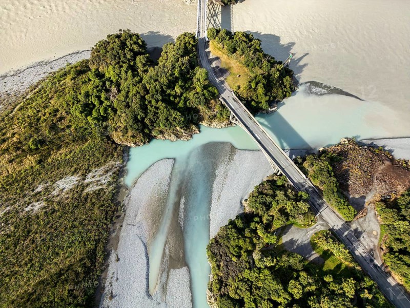 Aerial view captures the scenic landscape of a river and bridge in Canterbury, New Zealand. Lush greenery contrasts with the clear waters, showcasing natural beauty from above