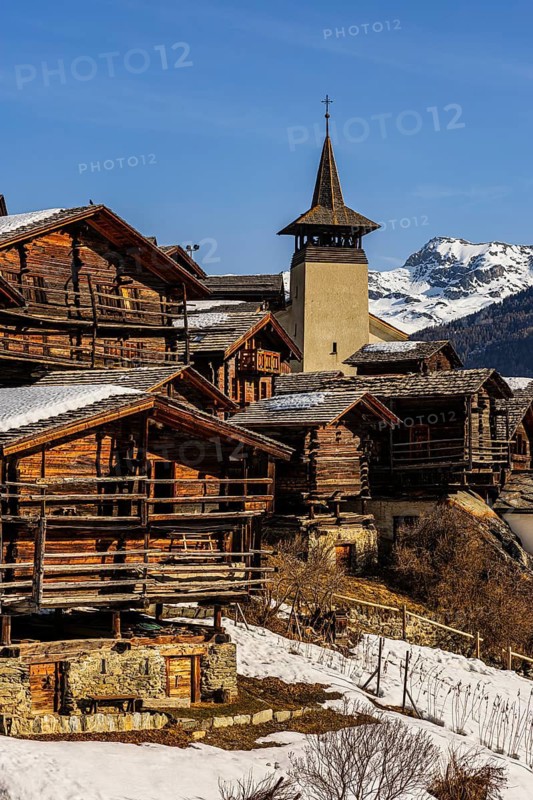Snow-covered roofs of old farmhouses and barn storage, in the back the church tower of the Saint Theodule church, historic town center, Grimentz, Val d'Anniviers, Valais Alps, Canton of Valais, Switzerland