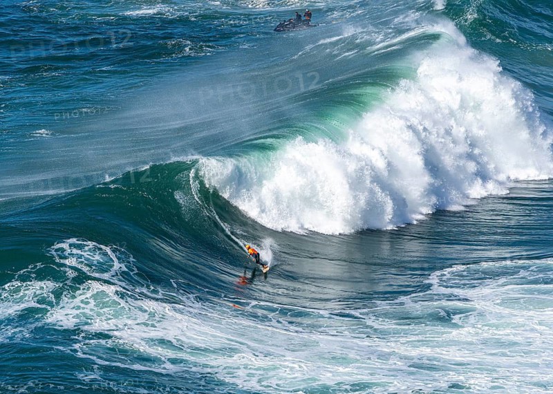 Surfers with their jet ski pilots in the Atlantic waves below Farol de Nazaré, Forte São Miguel, known as a surfer hot spot with monster waves between November and February of each year, Nazaré, Portugal