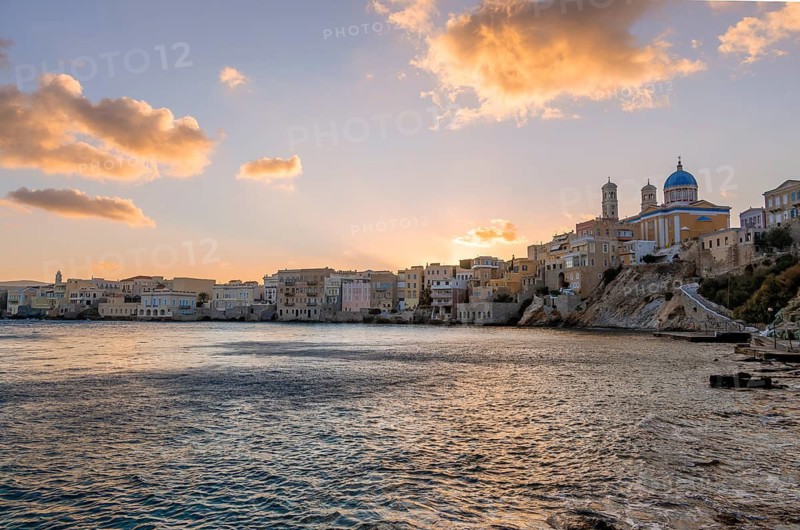View of the village with the Greek Orthodox church of Agios Nikolaos, Asteria Beach, at sunset with atmospheric clouds, Ermoupoli, Syros, Cyclades, Greece