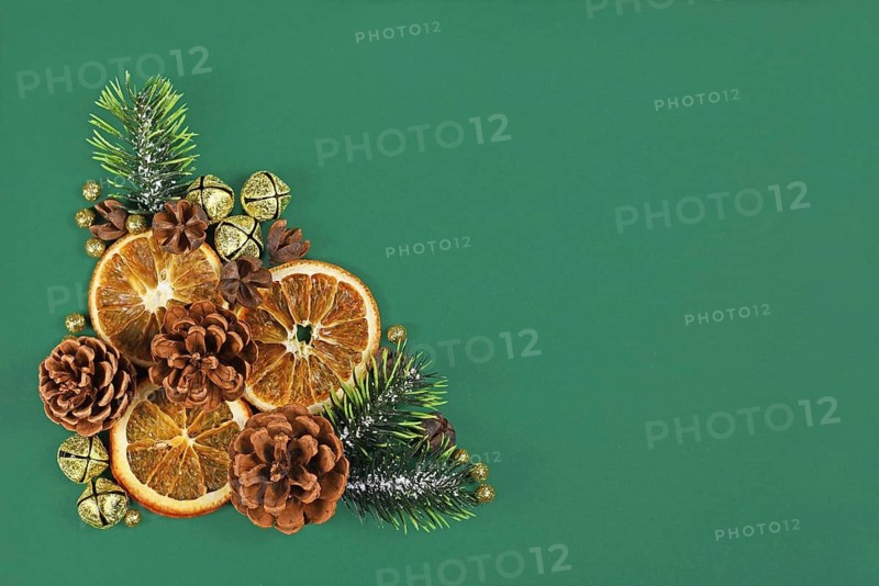Christmas arrangement with dried orange slices, fir branches and cones and golden bells on dark green background with empty copy space