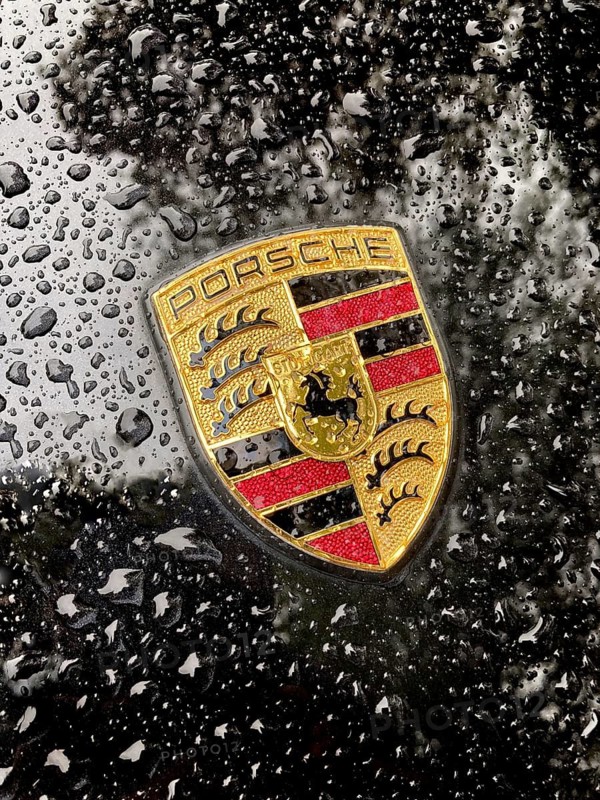 Porsche crest on black bonnet of sports car with sparkling raindrops, international