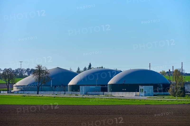 Agricultural biogas plant with three domes in green surroundings under blue sky, Middle Franconia, Bavaria, Germany