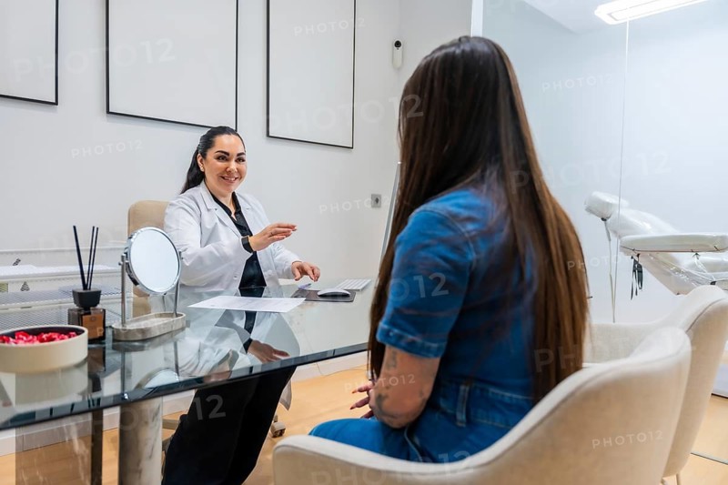 Female doctor in white coat talking with a patient during a consultation in a modern aesthetic clinic, discussing beauty treatments and medical spa services
