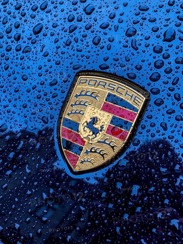 Porsche crest on navy blue bonnet of sports car with sparkling raindrops, international