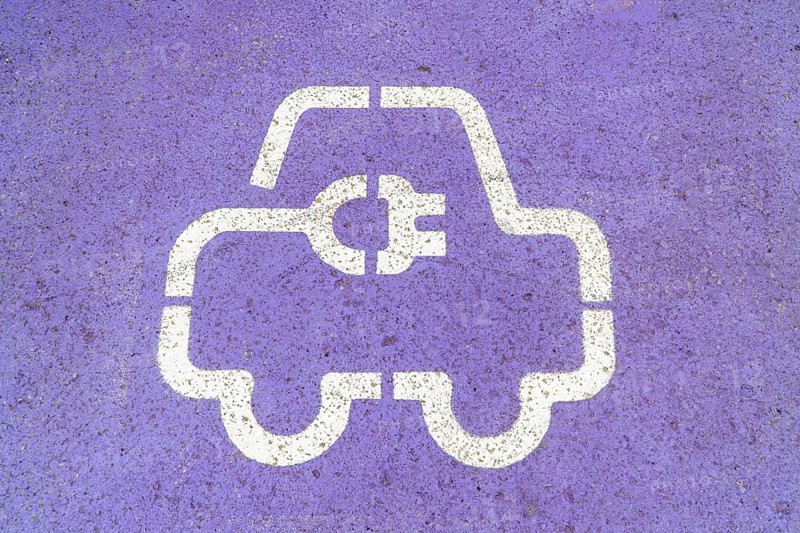 Close-up of a white electric vehicle EV charging station symbol painted on a purple asphalt surface, highlighting eco-friendly transportation
