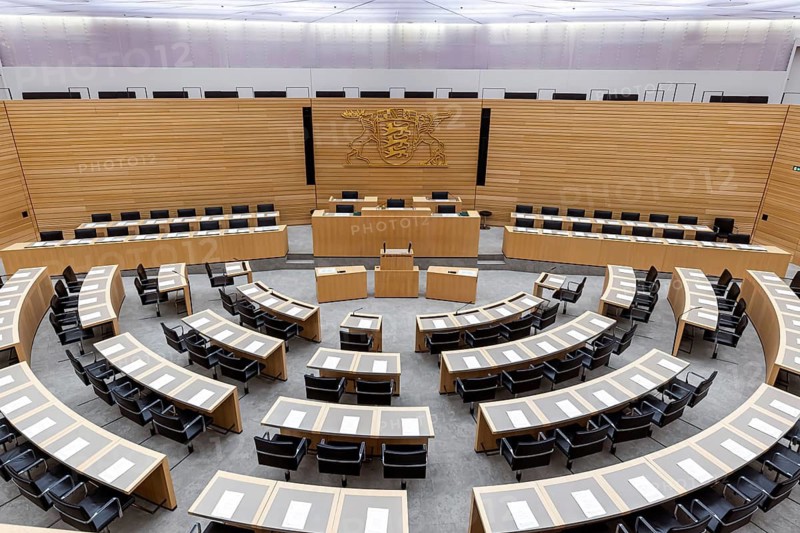 Plenary hall deserted with the seats of deputies and the government bank. Behind it is the coat of arms of the federal state. The state parliament of Baden-Württemberg is the state parliament based in Stuttgart, Baden-Württemberg, Germany