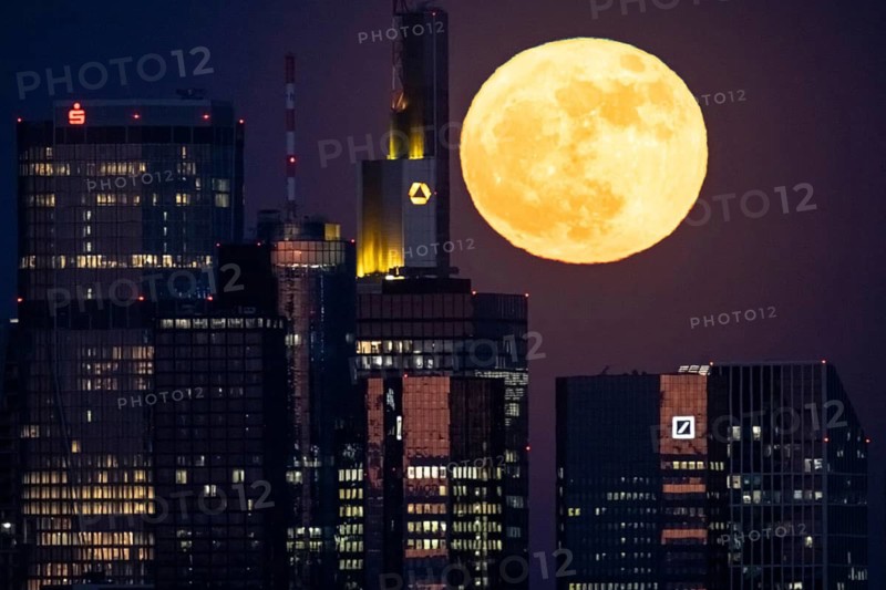 The full moon passes behind the Frankfurt banking skyline, Frankfurt am Main, Hesse, Germany