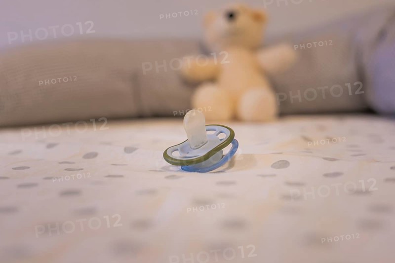 A pacifier lies in the foreground of a patterned sheet with a cuddly toy in the background, infants and toddlers daycare, Gechingen, Germany