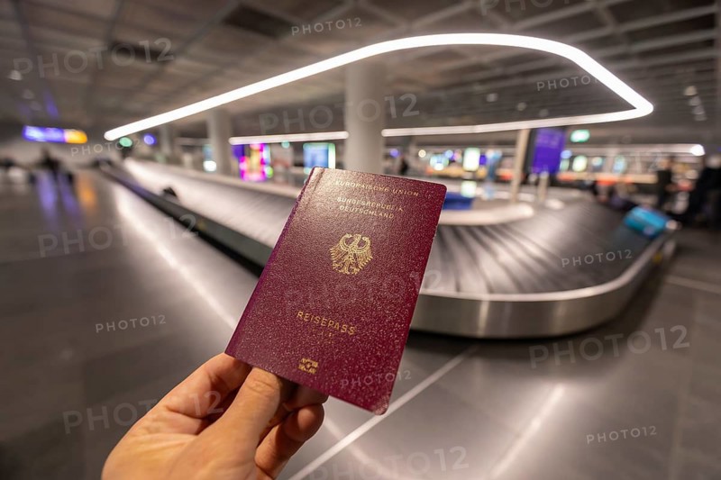 12.03.2026 hand holding German passport with baggage carousel in background at airport terminal, travel context at Frankfurt Airport, Hesse, Germany