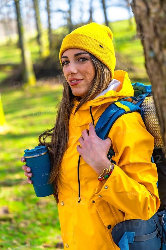Hiker enjoying a hot drink in the woods during a trekking day, wearing yellow raincoat and backpack