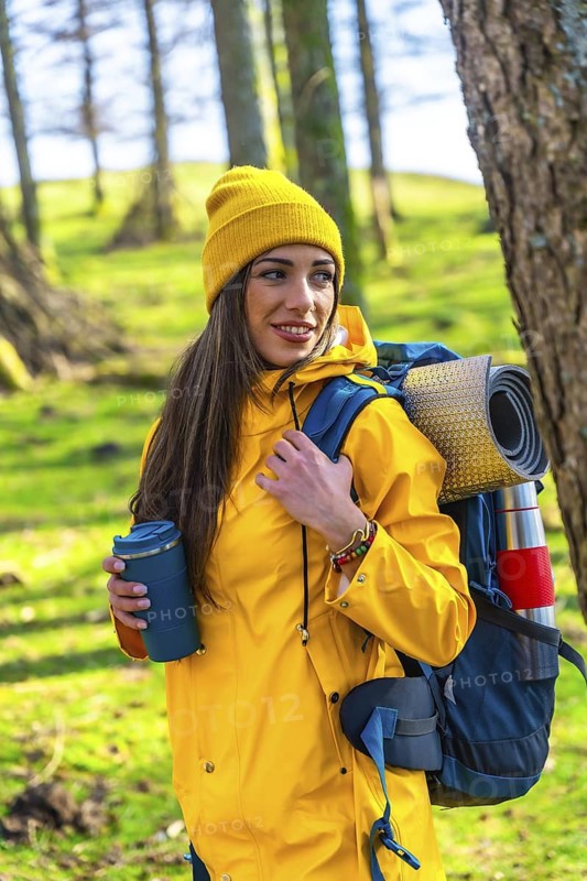Smiling hiker woman carrying backpack and thermos, enjoying trekking in forest during sunny day
