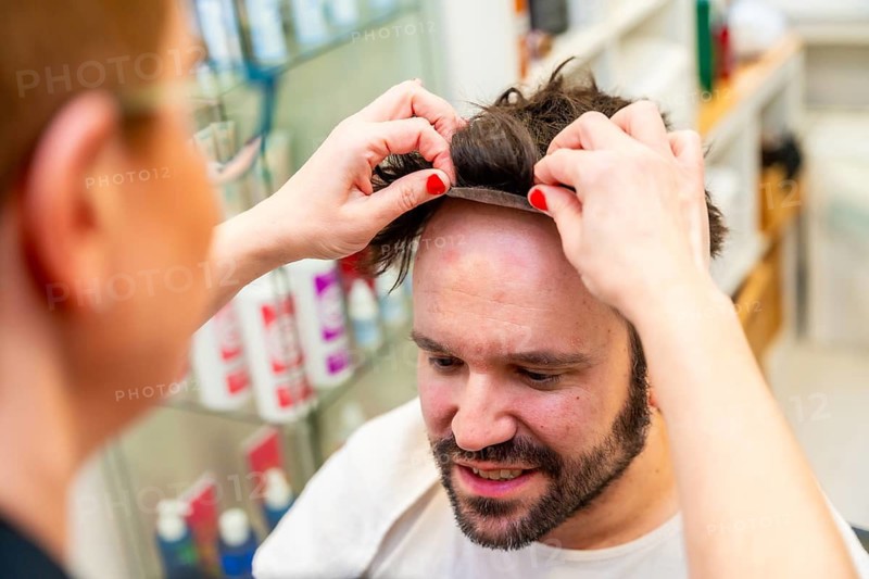Close-up top view of a hairdresser placing a capillary prosthesis carefully to a man's head