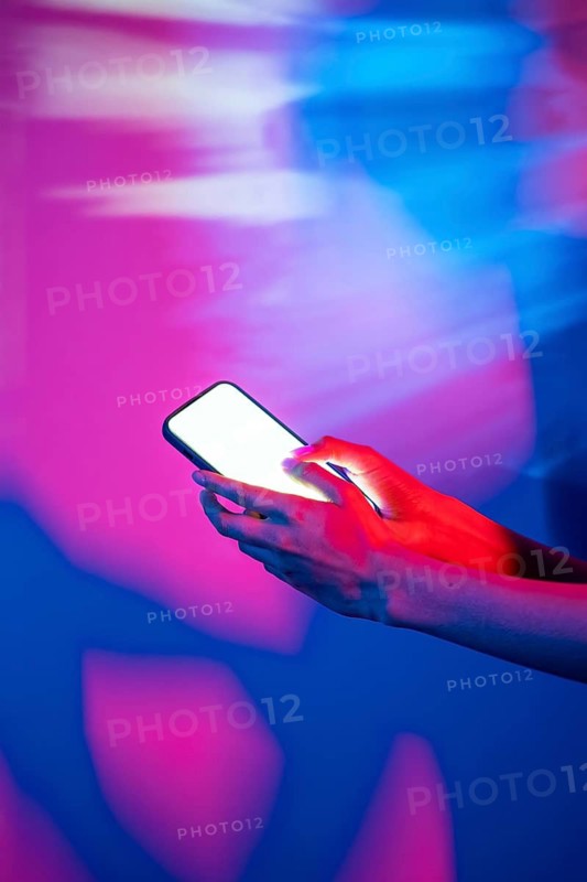 A hand interacts with a smartphone, illuminated by vibrant neon lights, creating a modern and futuristic atmosphere. Perfect for themes related to technology and nightlife