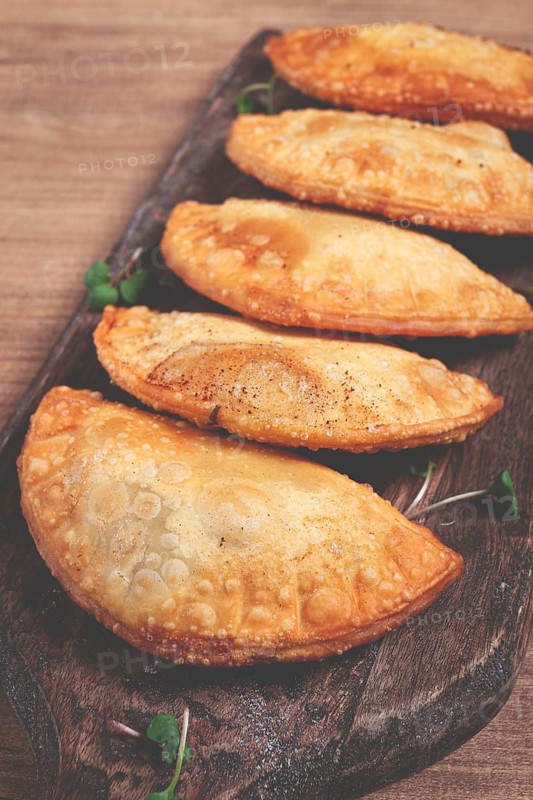 Fried chebureks, deep-fried, mini, on a chopping board, wooden table, close-up, no people