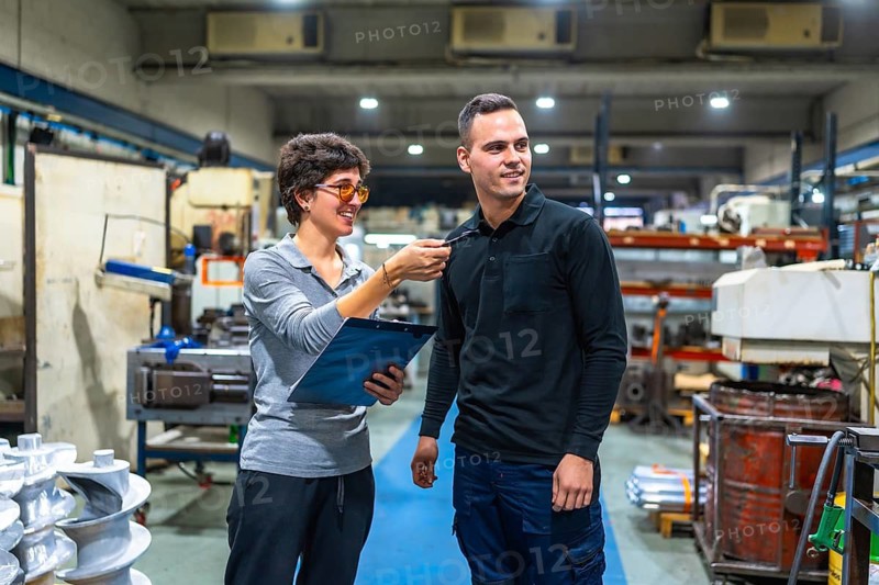 Female manager of factory talking and giving orders to male worker while holding clipboard