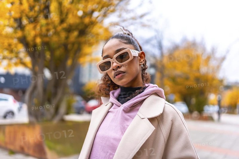 Cool african woman in coat and urban sunglasses standing in the street on a cold day of autumn