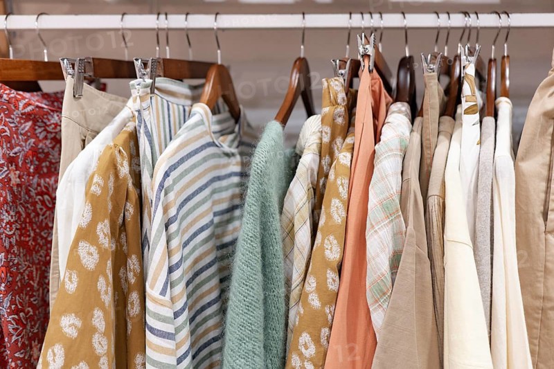 A collection of colorful clothes displayed on hangers of a clothes shop, featuring various textures and patterns. Ideal for fashion, retail, or organization themes