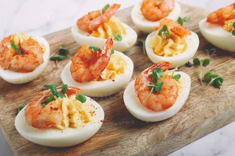Boiled eggs stuffed with yolk and seasoned with mayonnaise, stuffed eggs with shrimp, on a wooden chopping board, selective focus, close-up, no people