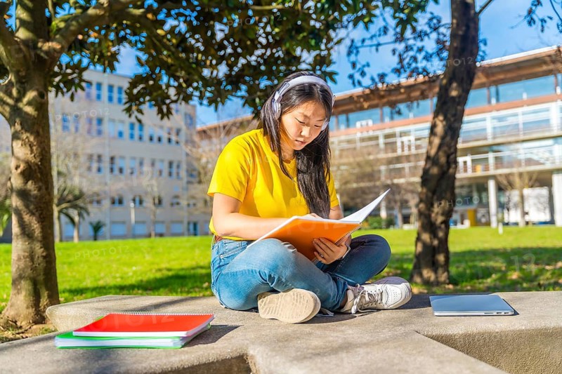 Serious chinese woman reading notes preparing an exam sitting outside the campus