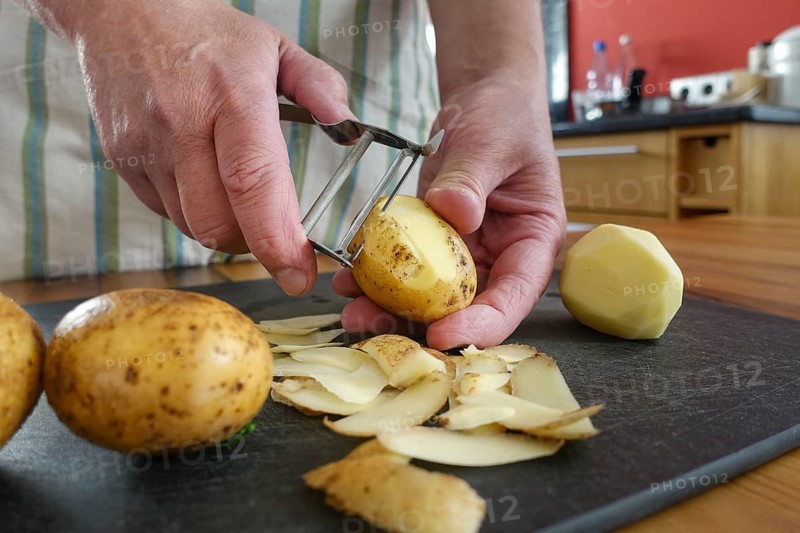Swabian cuisine, preparation of potato salad, peeling raw potatoes, savoury, salty, typical Swabian, typical Christmas dinner, quick cuisine for Christmas Eve, home cooking, traditional cuisine, men's hands, asparagus peeler, vegetable peeler, cutting board, food photography, studio, Germany