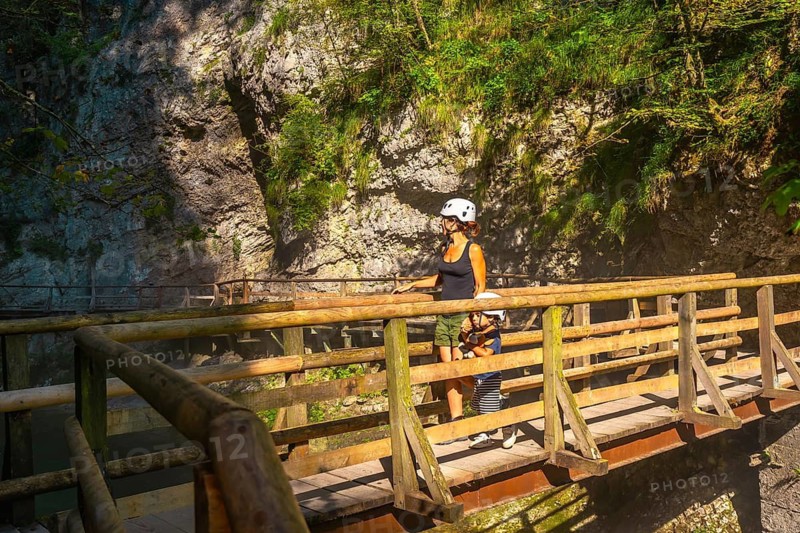 Mother and child wearing helmets are walking on a wooden bridge, enjoying the natural beauty of vintgar gorge near bled, slovenia