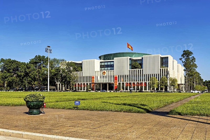 Modern building with glass fronts, flags and surrounding lawn under a clear sky, building of the Vietnamese National Assembly in Hanoi Vietnam
