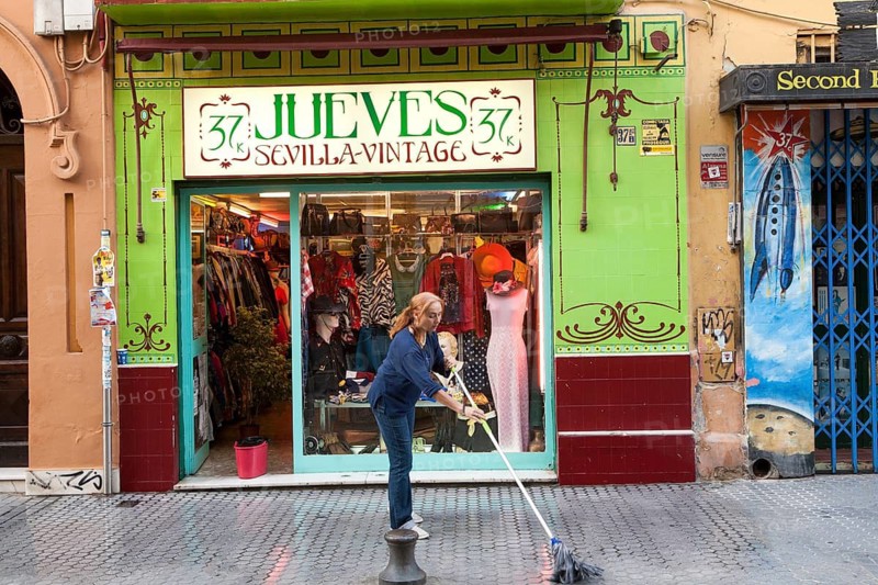 Woman mopping the street outside Jueves vintage clothes shop in Barrio Macarena, Seville, Spain