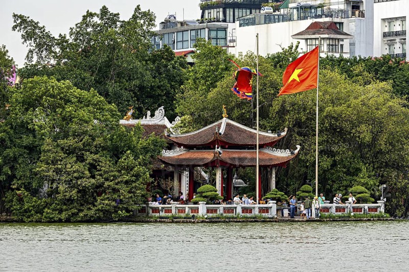 Traditional temple in Vietnam by the lake with trees in the background, Vietnamese flag waving, The Ngoc Son Temple in Hoan Kiem Lake in Hanoi Vietnam