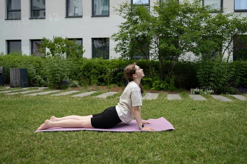 A teen girl performs a yoga pose on a purple mat in a green backyard, focusing on relaxation and mindfulness. She enjoys the peaceful outdoor environment