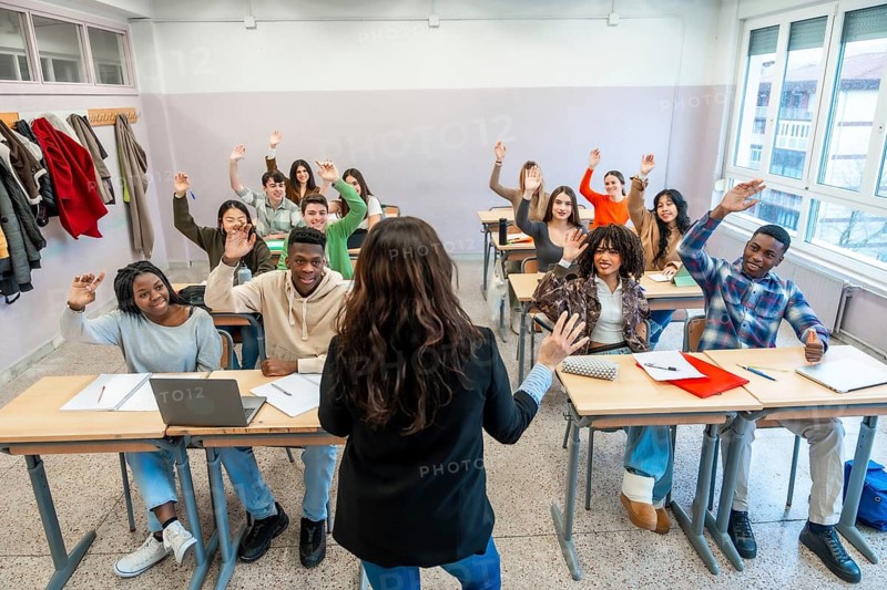 Multi ethnic university students enthusiastically raising hands to respond to the teacher's questions during an engaging classroom lesson