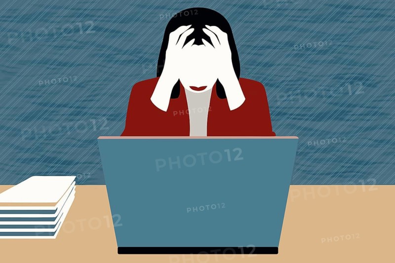 A businesswoman sits at her desk, visibly stressed and frustrated with her laptop in front of her. She holds her head in her hands, conveying feelings of depression
