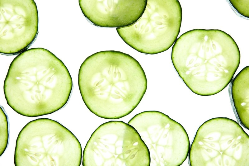 Slices of fresh cucumber are arranged on a light background, showcasing their crisp texture and vibrant green color. Ideal for healthy eating or skincare concepts