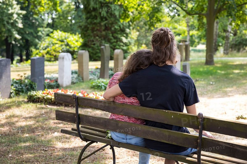 Young couple sitting on a bench between graves, Riesa Cemetery, Saxony, Germany